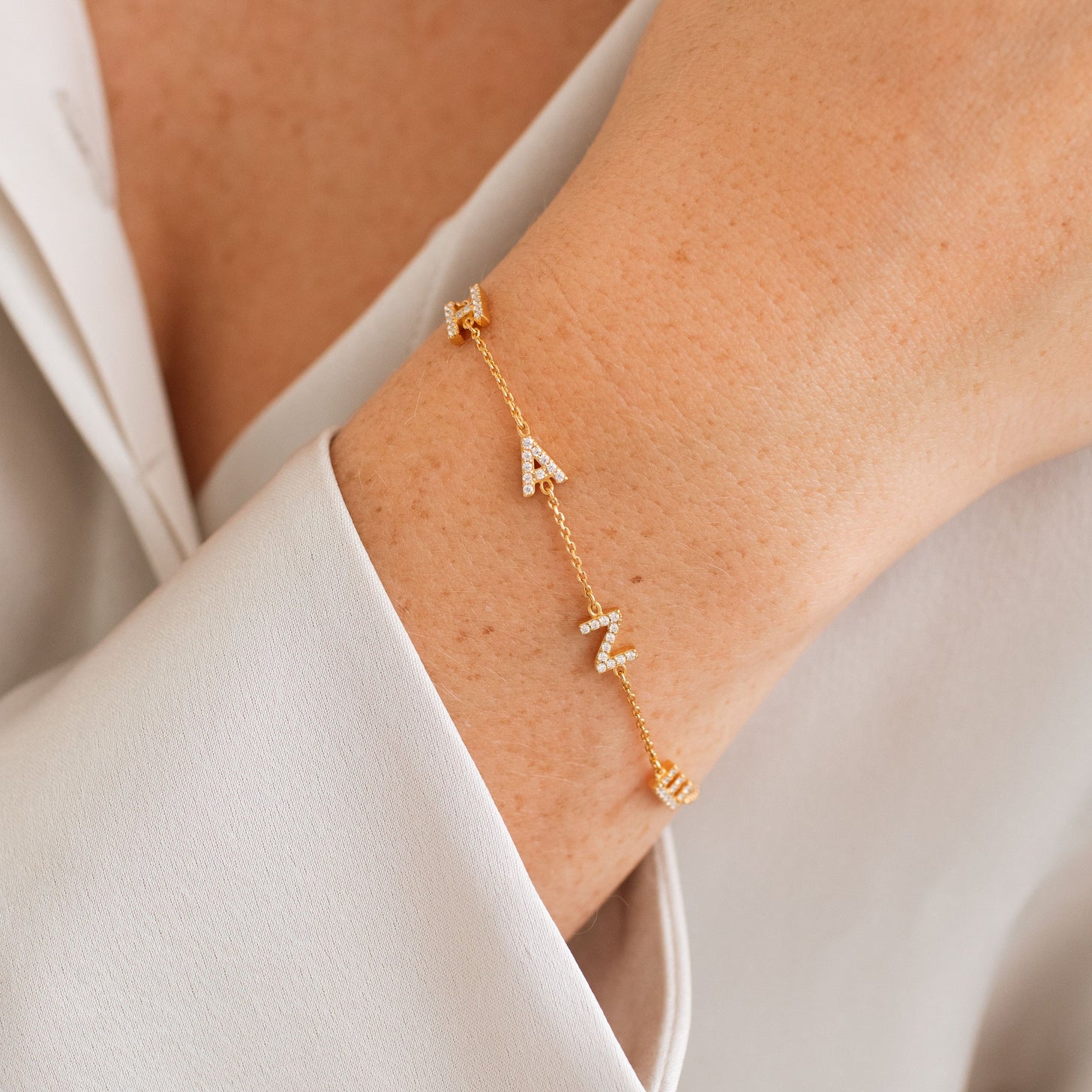 Model wearing gold sideways letters bracelet with custom short name and numbers
