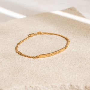 A gold custom engraved bracelet with a long bar and curb chain