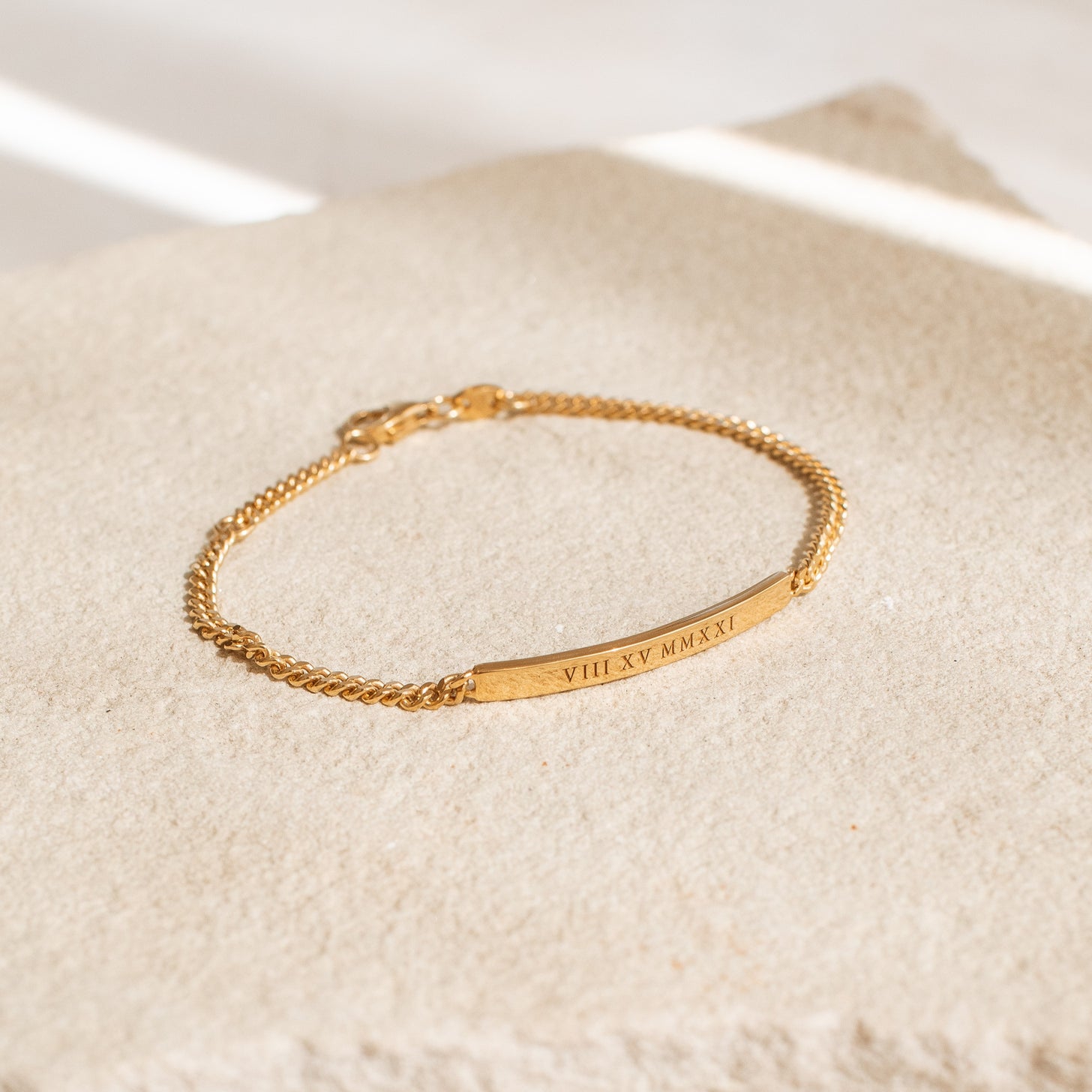 A gold custom engraved bracelet with a long bar and curb chain