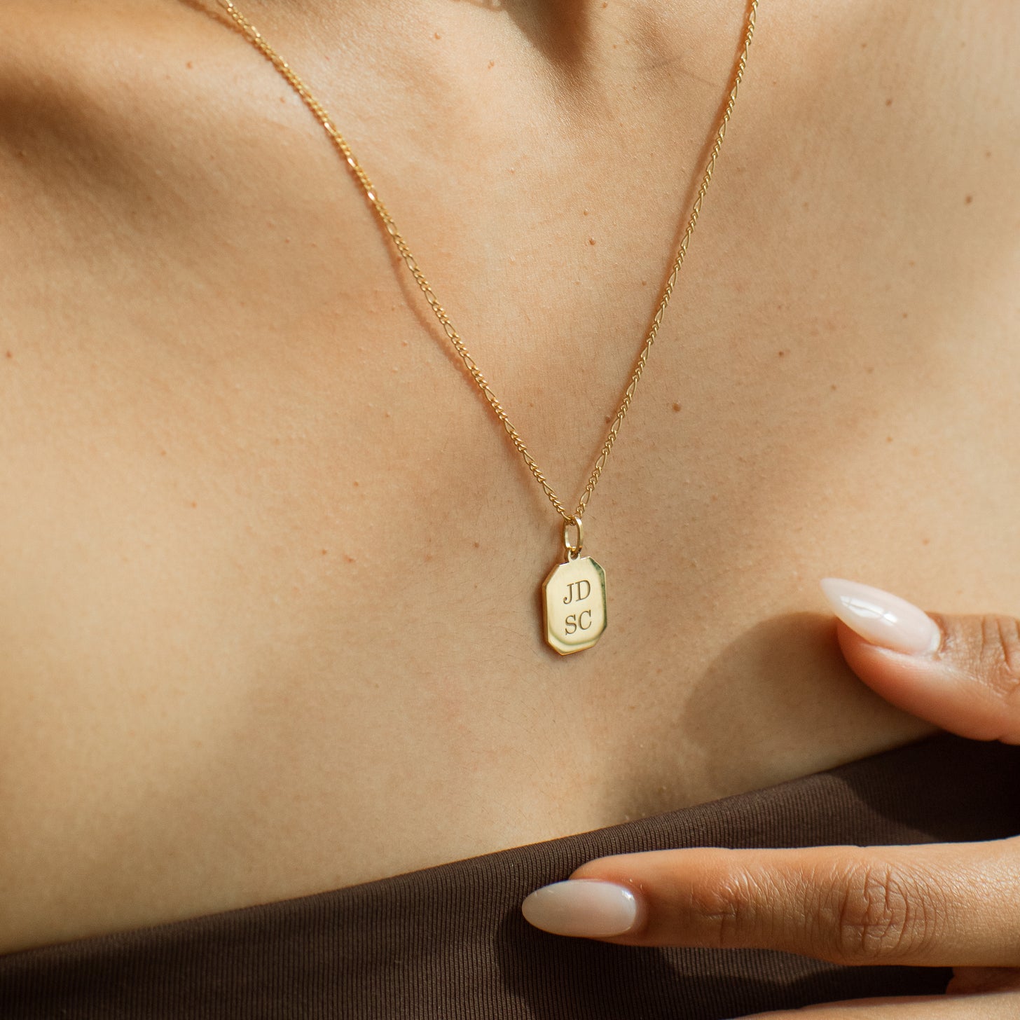 4 initials engraved on a gold dog tag pendant necklace. This necklace can be engraved on both sides in a modern font or a romantic script font