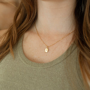 Personalized initial engraving on a gold dog tag pendant necklace in an elegant modern font