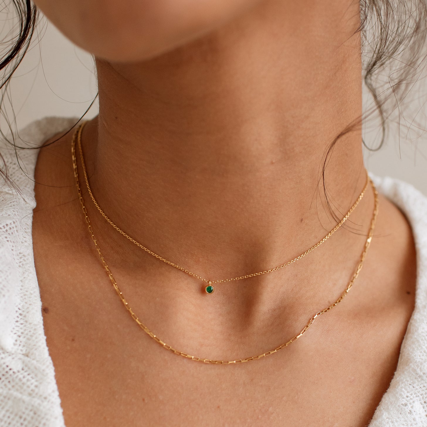 Model wears a dainty emerald birthstone necklace, layered with a mini link chain necklace