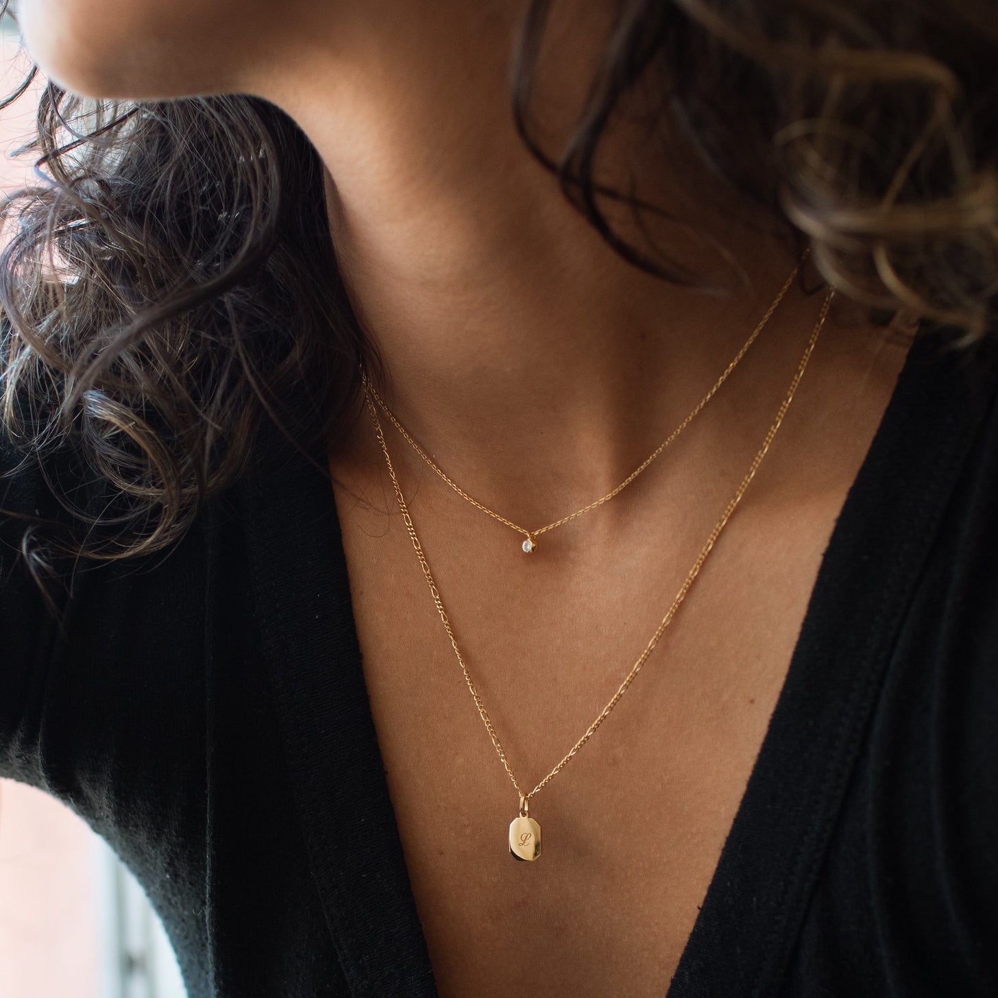 Model wears a dainty white sapphire birthstone necklace layered with a pendant necklace