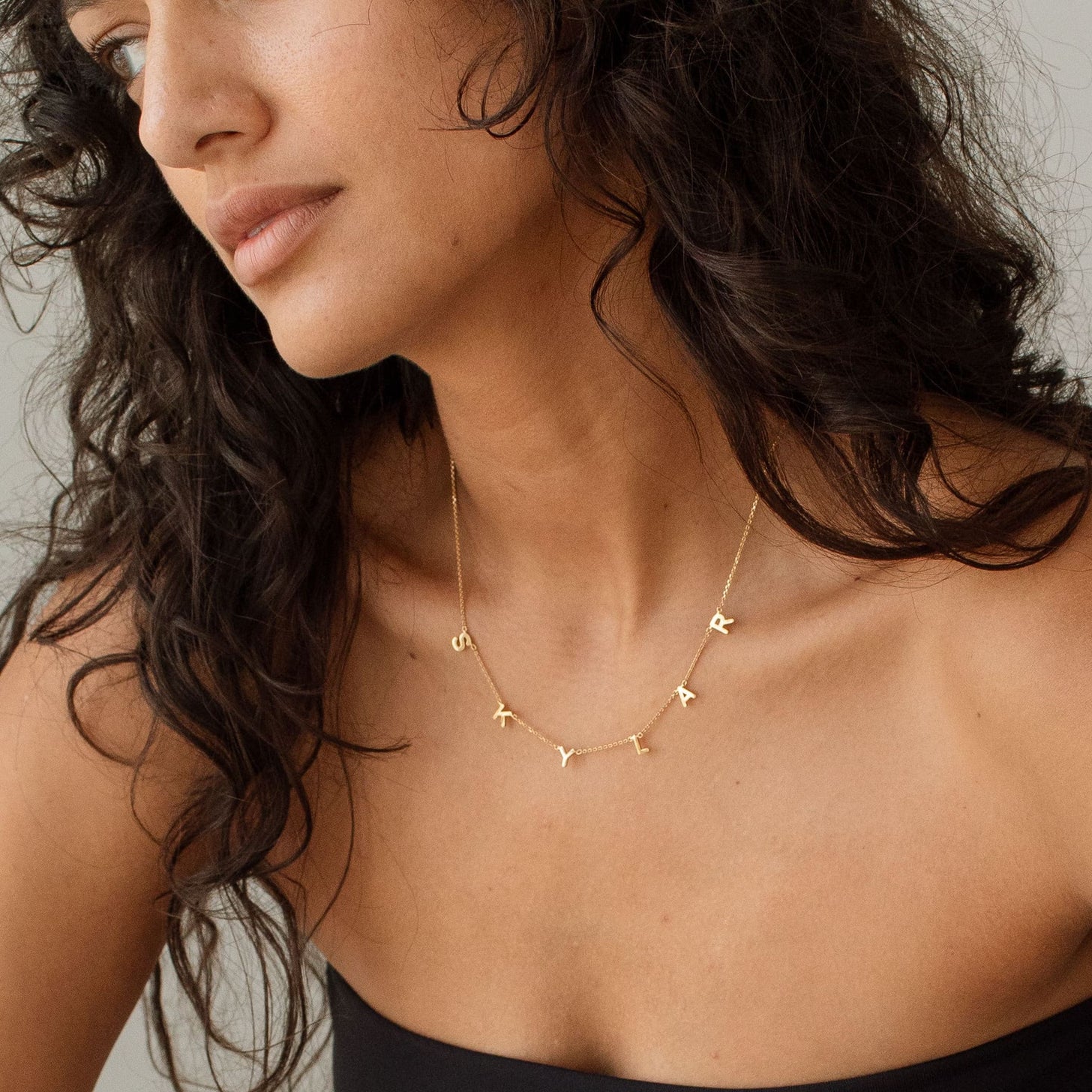 Woman wearing a gold name necklace with a neutral background