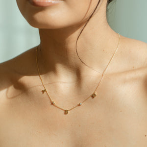 Model wearing a dainty initials necklace featuring stones along a cable chain