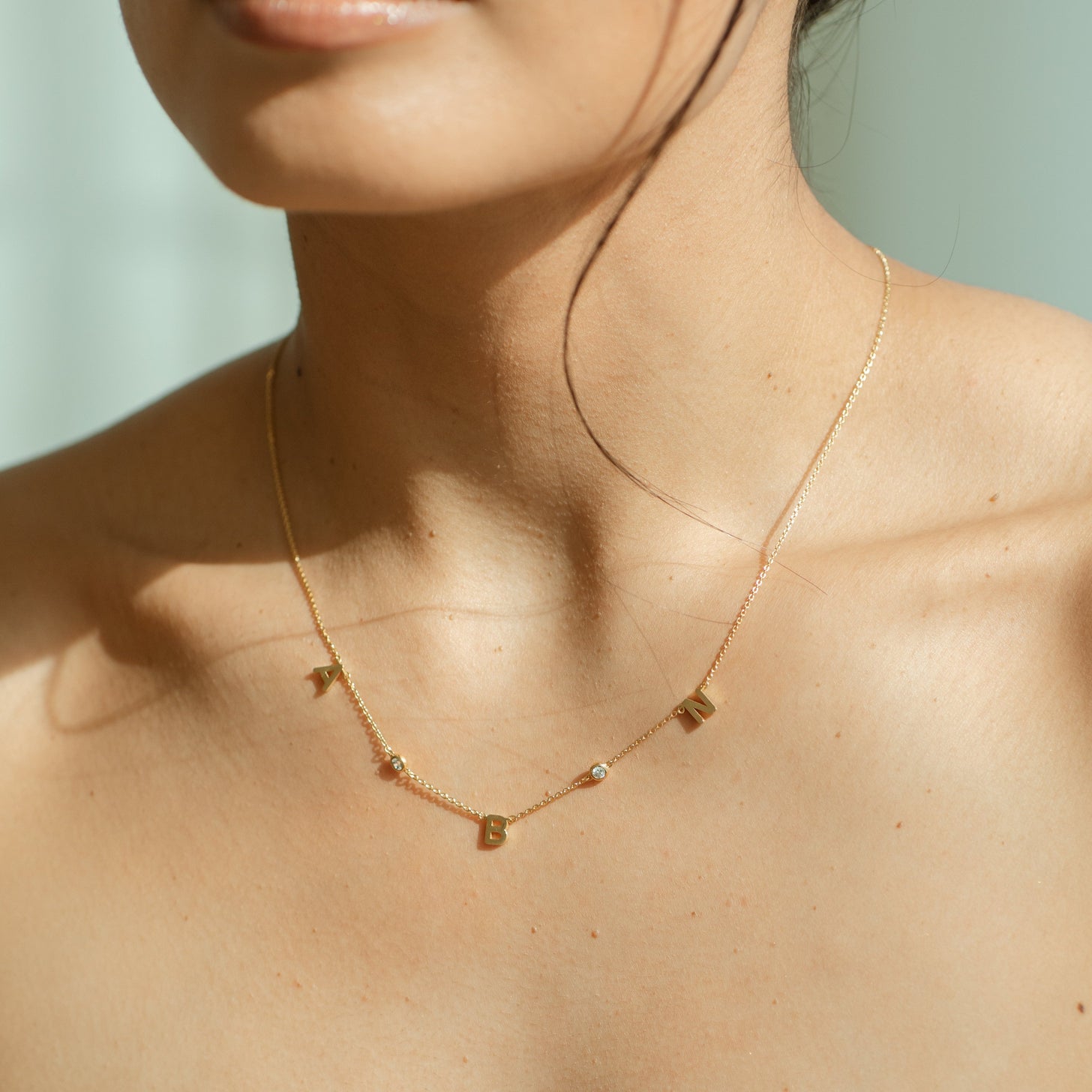 Model wearing a dainty initials necklace featuring stones along a cable chain