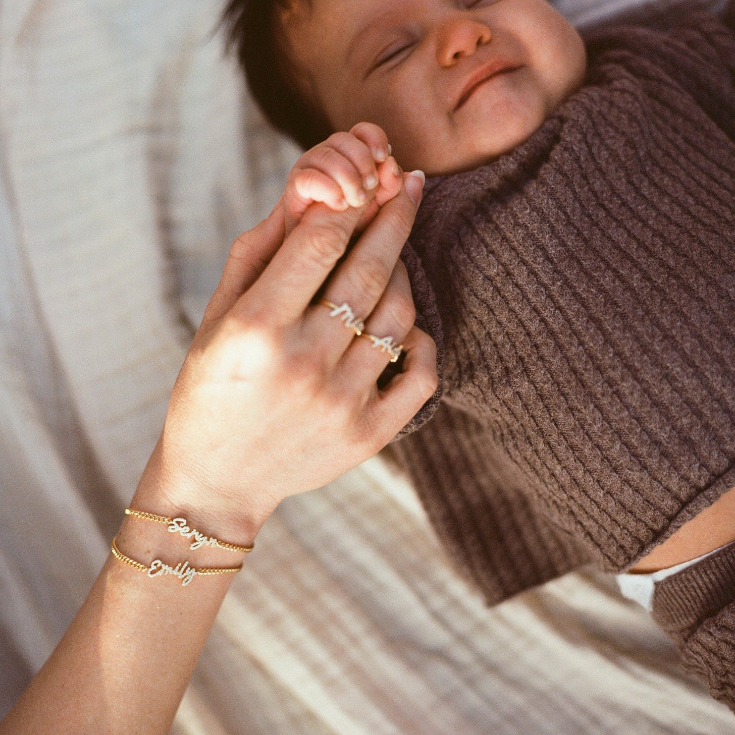Woman holding baby's hand wearing Naia Name Bracelets and rings