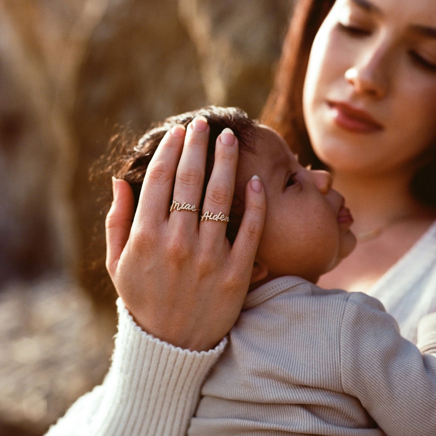 Mother holding baby wearing Naia Name Rings studded in cubic zirconia stones