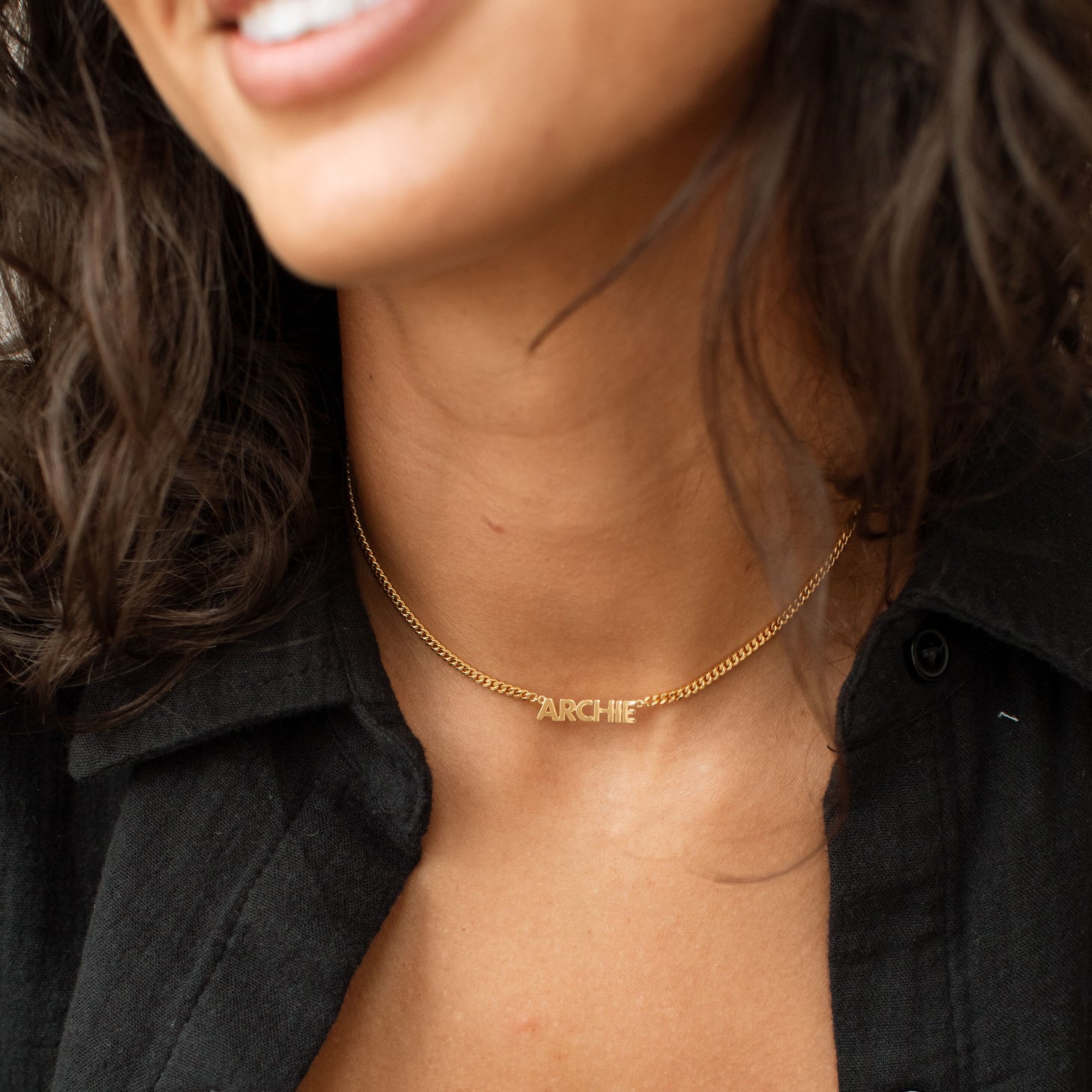 Model wearing a gold Nelly Name Necklace with black button down shirt
