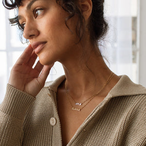 Model wearing 2 gold Noah Name Necklaces with sweater