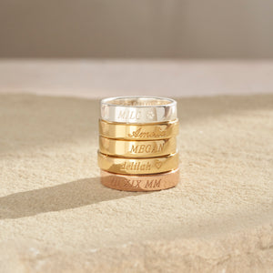 Custom engraved band rings in silver, gold, and rose gold are stacked, showing the elegant italic and cursive fonts