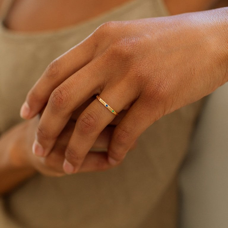 Model wears a dainty gold band ring with custom engraved names and birthstones