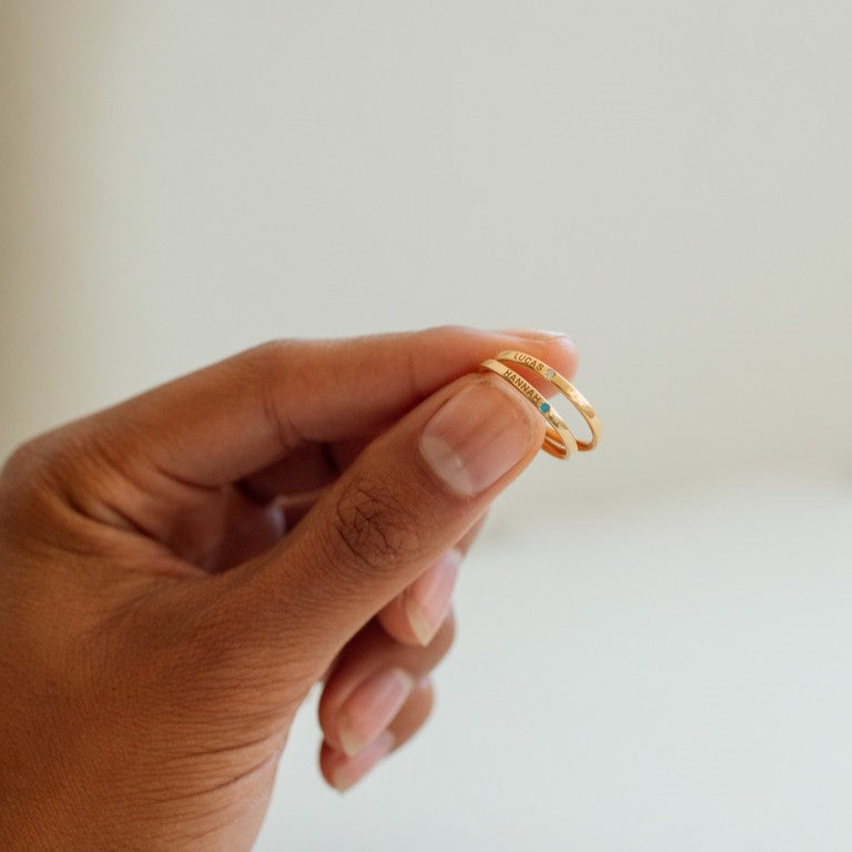 Dainty gold band rings featuring birthstones and personalized engravings on the outer and inner band